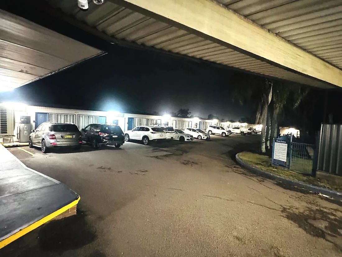 The motel court at night, cars parked directly outside the room doors under the lit awning.