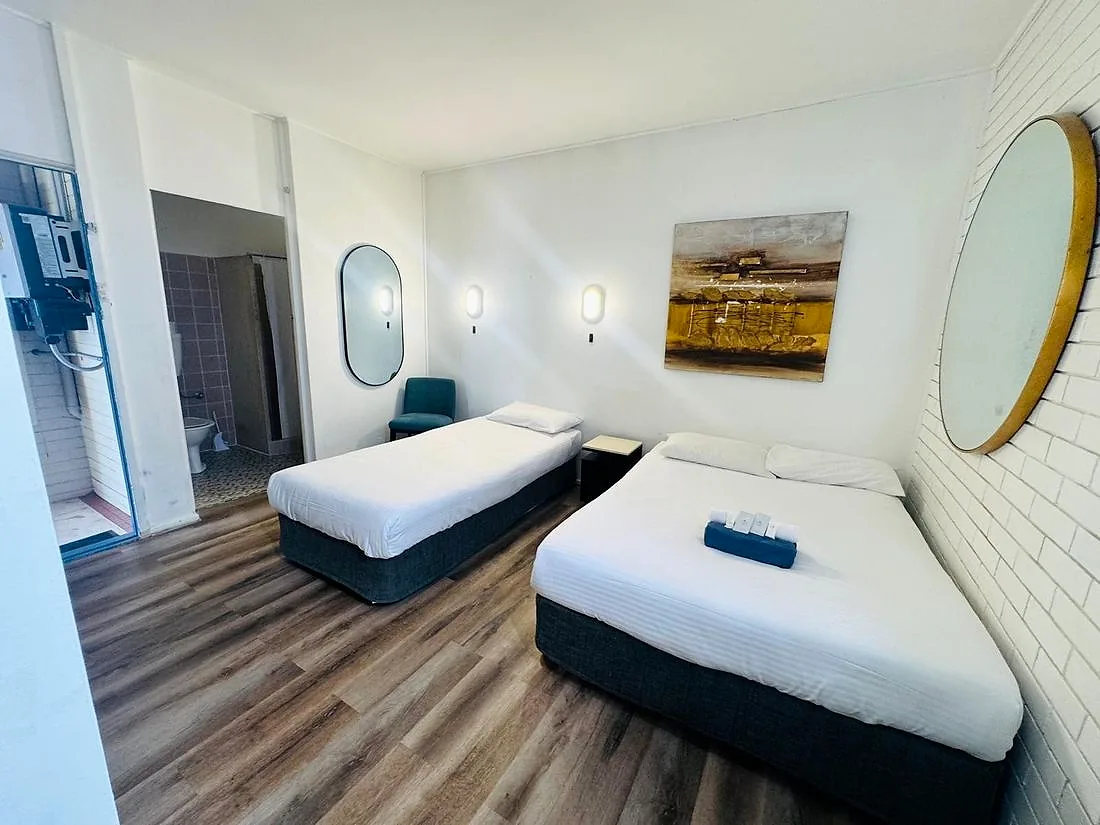 Refurbished Standard Twin room at Mayfield Motel — two single beds, painted white brick, timber-look flooring, oval and round mirrors, ensuite visible through the doorway.